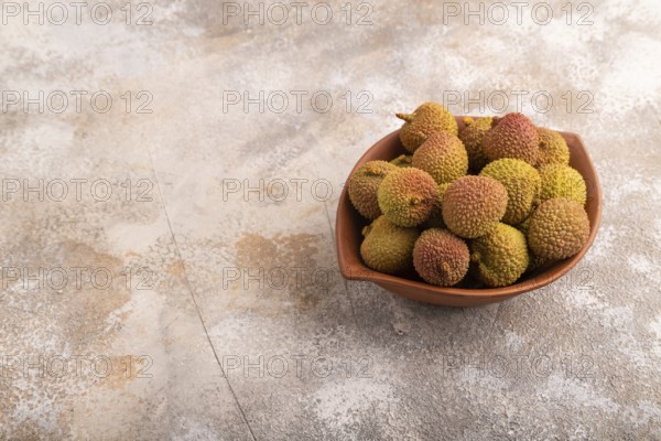 Ripe Lychee on clay bowl on brown concrete background, side view, copy space, minimalism