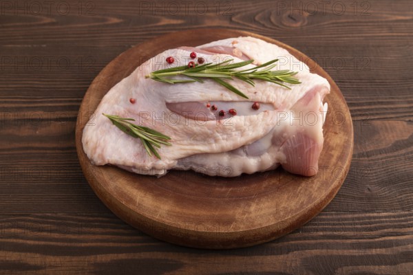 Raw Turkey Thigh with spices and rosemary on cutting board on brown wooden background. side view, close up