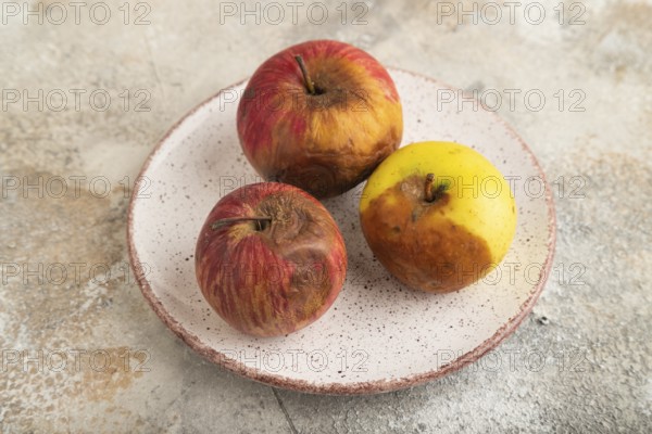 Decaying, Rotting apples on ceramic plate on brown concrete background. Side view, close up, minimalism