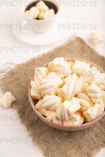 Orange and pink marshmallow in ceramic bowl on white wooden background, side view, close up, minimalism, selective focus