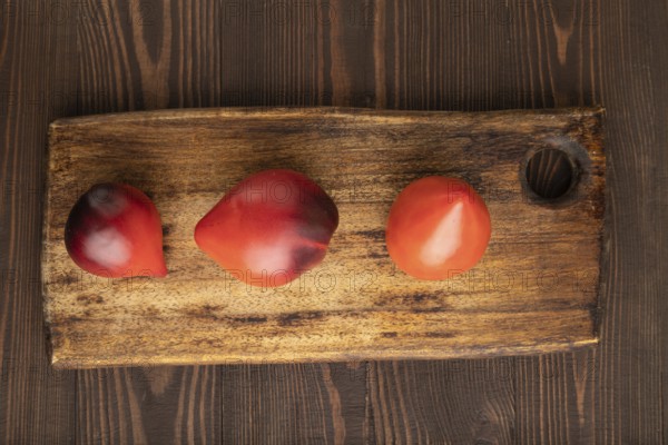 Red Heart shape tomatoes on cutting board on brown wooden background. Top view, copy space, flat lay. healthy food, vegetable, minimalism