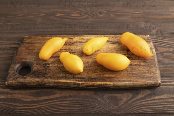 Yellow tomatoes on cutting board on brown wooden background. Side view, copy space. healthy food, vegetable, minimalism