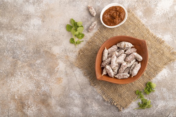 Small smoked Chicken sausages in clay bowl on brown concrete background and linen textile. top view, flat lay, copy space