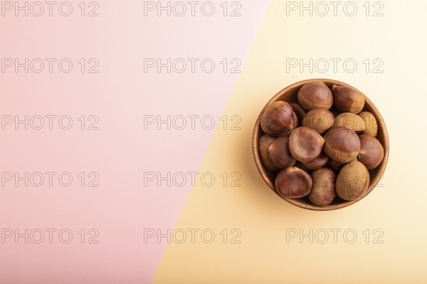 Wooden bowl with raw edible ?hestnuts on pink and orange paper pastel background, top view, flat lay, copy space, minimalism