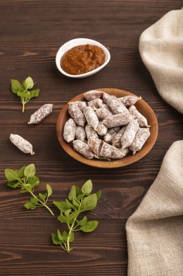 Small smoked Chicken sausages in wooden bowl on brown wooden background and linen textile. side view, close up