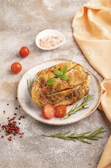 Fried Turkey Thigh with spices and rosemary on plate on brown concrete background and orange linen textile. side view, close up