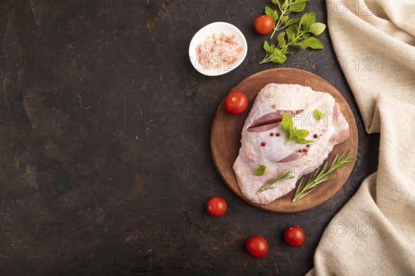 Raw Turkey Thigh with spices and rosemary on cutting board on black concrete background and linen textile. top view, flat lay, copy space