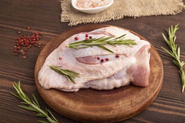 Raw Turkey Thigh with spices and rosemary on cutting board on brown wooden background and linen textile. side view, close up