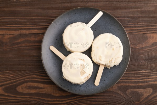 ?hocolate Ice cream in white glaze, on brown wooden background, top view, flat lay, close up