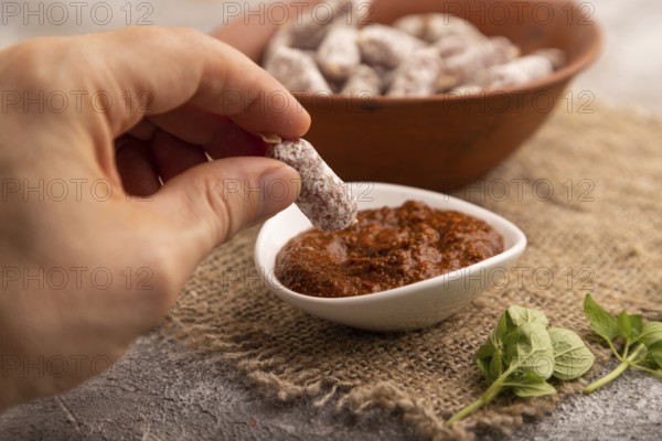 Small smoked Chicken sausages in clay bowl with hand on brown concrete background and linen textile. side view, close up, selective focus