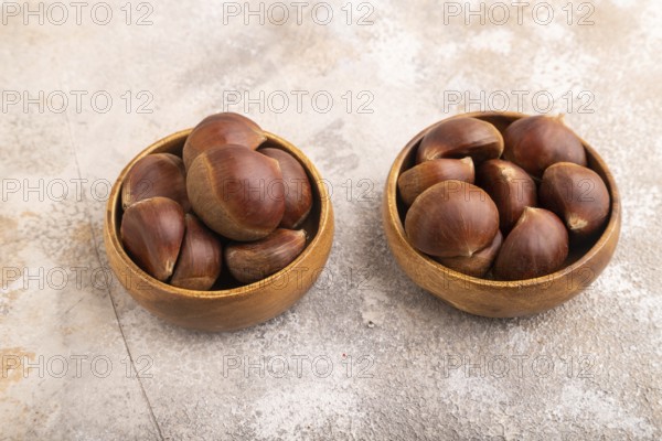 Wooden bowl with raw edible ?hestnuts on brown concrete background, side view, close up, minimalism