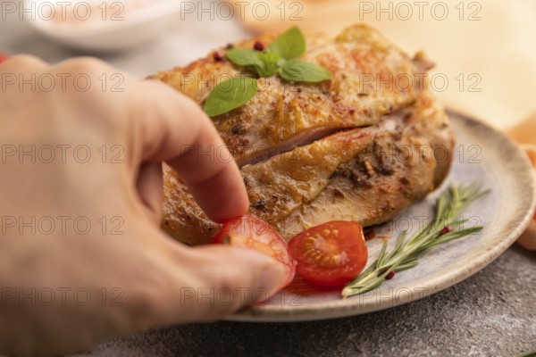 Fried Turkey Thigh with spices and rosemary on plate with hand on brown concrete background and orange linen textile. side view, close up, selective focus