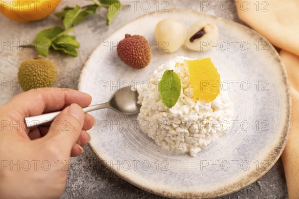 White ?ottage cheese, Curd, with orange and lychee with hand on brown concrete background and orange textile, side view, close up, selective focus