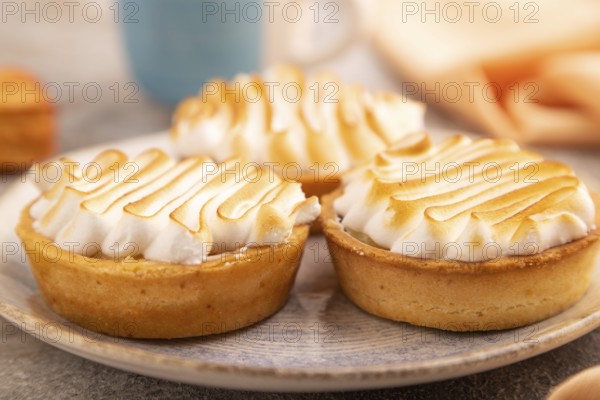 French lemon tart with meringue on brown concrete background, cup of coffee, orange linen textile, side view, close up, selective focus