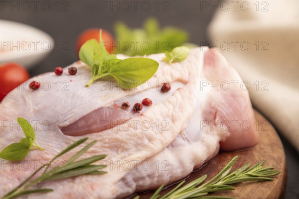 Raw Turkey Thigh with spices and rosemary on cutting board on black concrete background and linen textile. side view, close up, selective focus