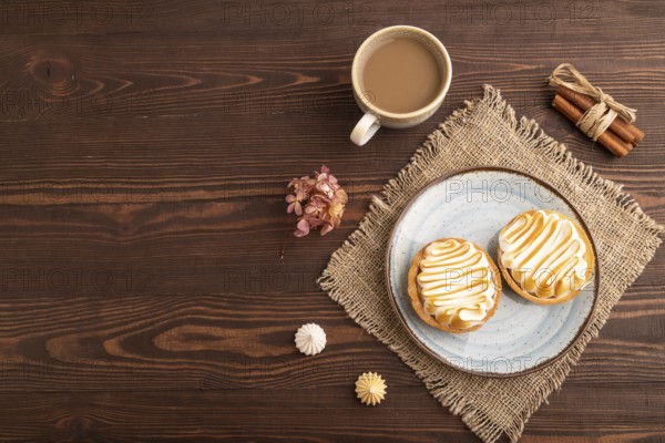 French lemon tart with meringue on brown wooden background, cup of coffee, linen textile, top view, flat lay, copy space