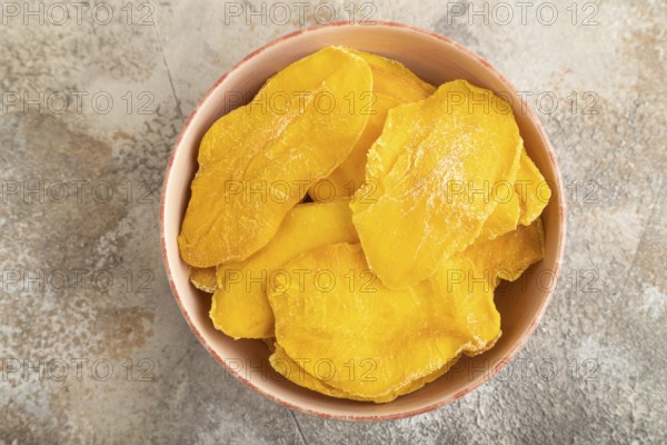 Dried Mango in ceramic bowl on brown concrete background. Top view, close up, flat lay. healthy food, minimalism