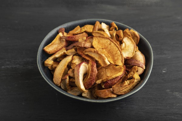 Dried Apples in ceramic bowl on black wooden background. Side view, close up. healthy food, minimalism. sweet