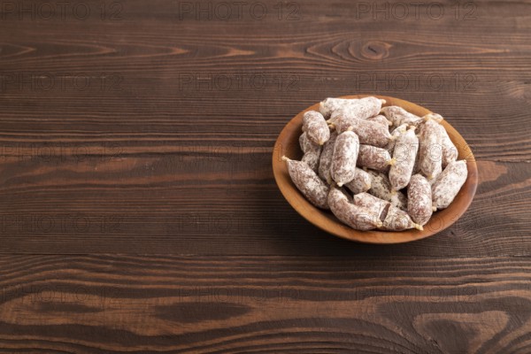 Small smoked Chicken sausages in wooden bowl on brown wooden background. side view, copy space