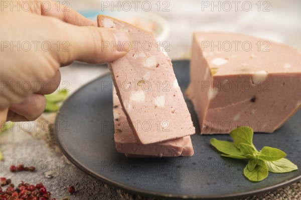 Mortadella sausage with hand on plate with pepper and herbs on brown concrete background and linen textile. Side view, close up, selective focus