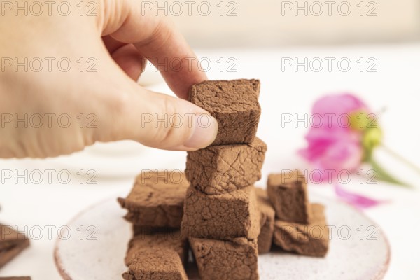 Chocolate marshmallow with cup of coffee with hand on white wooden background. side view, close up, selective focus
