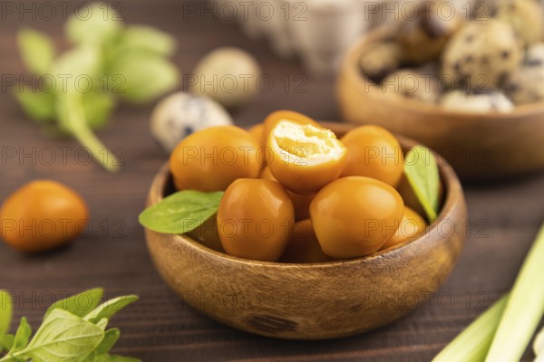 Pile of Smoked Quail eggs in bowl on a brown wooden background. side view, close up, selective focus