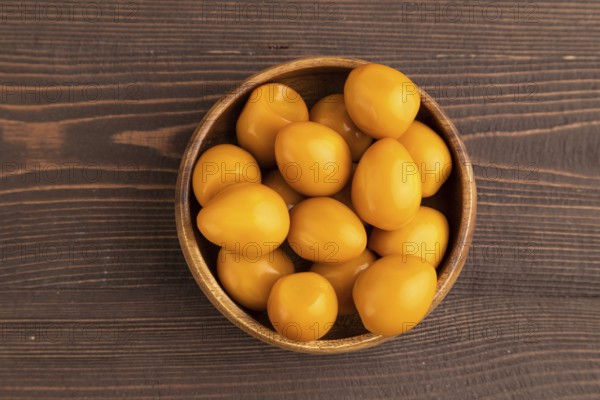 Pile of Smoked Quail eggs in bowl on a brown wooden background. top view, flat lay, close up