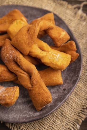 Crunchy biscuit Brushwood cookies sprinkled with powdered sugar on brown wooden background and linen textile, cup of coffee, side view, close up, selective focus