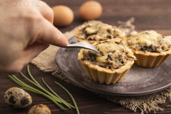 Tartlets with meat and cheese with hand on brown wooden background and linen textile. side view, close up, selective focus