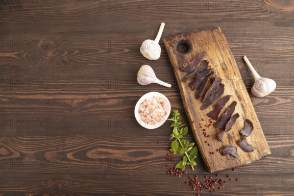 Armenian Basturma dried meat on wooden cutting board with pepper and herbs on brown wooden background. Top view, flat lay, copy space
