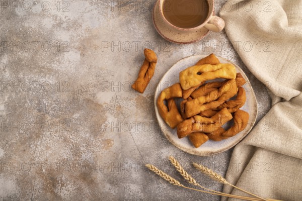 Crunchy biscuit Brushwood cookies sprinkled with powdered sugar on brown concrete background and linen textile, cup of coffee, top view, flat lay, copy space