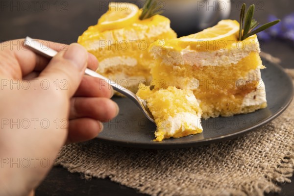 Lemon cake with hand on black concrete background and linen textile, cup of coffee, side view, close up, selective focus