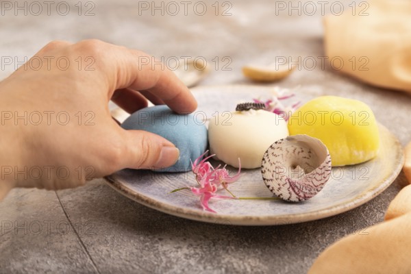 Japanese Mochi Cakes with hand on brown concrete background and orange textile, side view, close up, selective focus