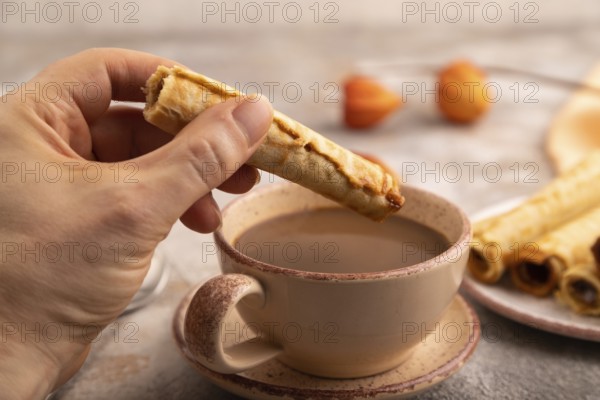 Waffles with caramel with hand on brown concrete background and orange linen textile, side view, close up, selective focus