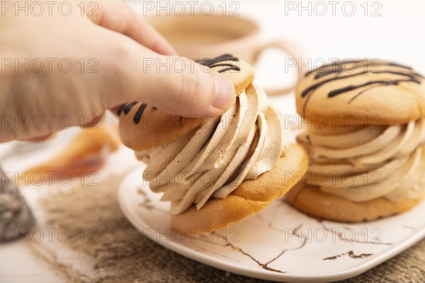 Caramel Cream Cakes with hand on white wooden background and linen textile, cup of coffee, side view, close up, selective focus