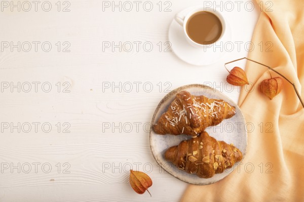 Croissant on blue plate on white wooden background and orange linen textile, cup of coffee, top view, flat lay, copy space