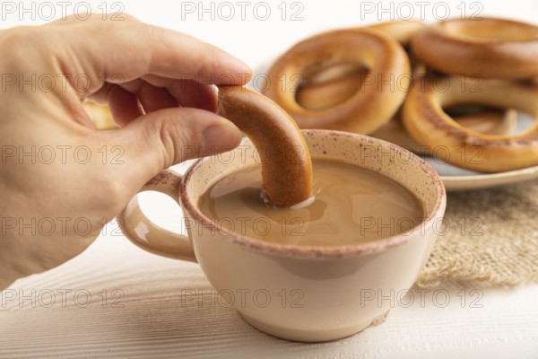 Homemade Ring Bagel with hand with cup of coffee on white wooden background and linen textile. side view, close up, selective focus