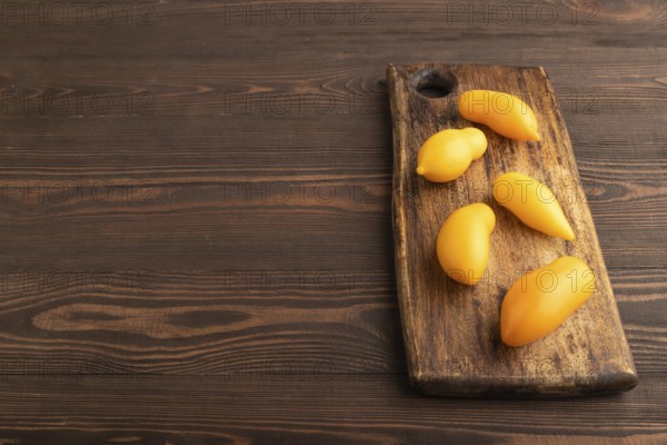 Yellow tomatoes on cutting board on brown wooden background. Side view, copy space. healthy food, vegetable, minimalism