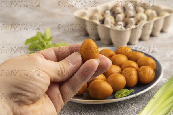 Pile of Smoked Quail eggs on plate with hand on a brown concrete background. side view, close up