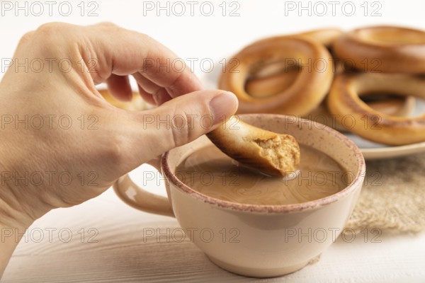 Homemade Ring Bagel with hand with cup of coffee on white wooden background and linen textile. side view, close up, selective focus