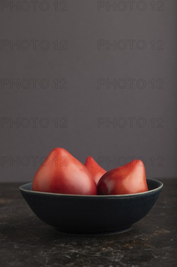 Red Heart shape tomatoes in blue bowl on black concrete background. Side view, copy space. healthy food, vegetable, minimalism, low key