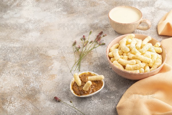 Corn flakes sticks with caramel in ceramic bowl on gray concrete background and orange linen textile. Side view, copy space