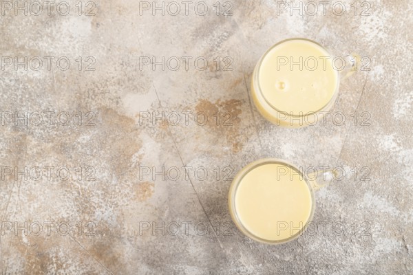 Organic non dairy banana and soy milk in glass on brown concrete background. Vegan healthy food concept, flat lay, top view, copy space