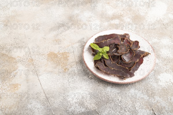 Armenian Basturma dried meat on plate with pepper and herbs on brown concrete background. Side view, copy space