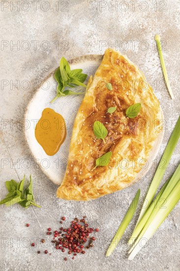 Fried homemade Khachapuri cake with cheese and meat, fried in pan. Traditional Georgian cuisine on brown concrete background. Top view, flat lay, close up