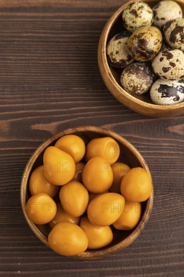 Pile of Smoked Quail eggs in bowl on a brown wooden background. top view, flat lay, close up