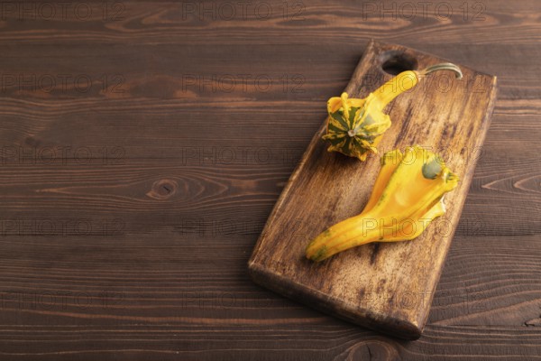 Decorative orange Pumpkin on cutting board on brown wooden background, side view, copy space, minimalism