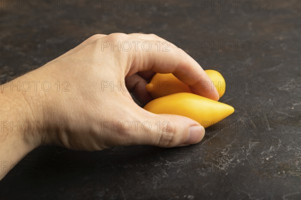 Yellow tomatoes with hand on black concrete background. Side view, copy space. healthy food, vegetable, minimalism. hold
