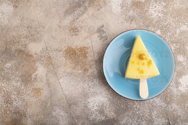 Yellow Cake pop with sprinkles on blue ceramic plate on brown concrete background, top view, flat lay, copy space, minimalism