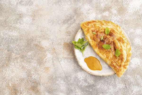 Fried homemade Khachapuri cake with cheese and meat, fried in pan. Traditional Georgian cuisine on brown concrete background. Side view, copy space